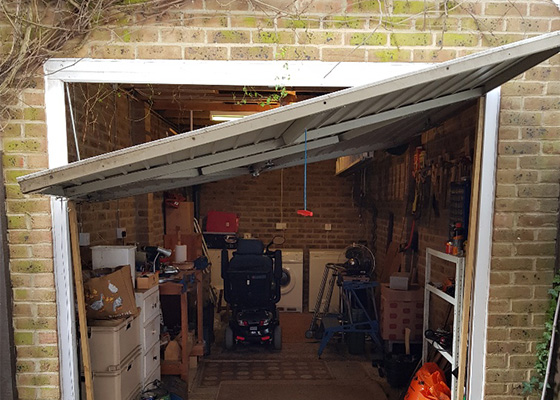damaged garage door with tools and equipment inside storage area showing mobility scooter and cluttered space for organization